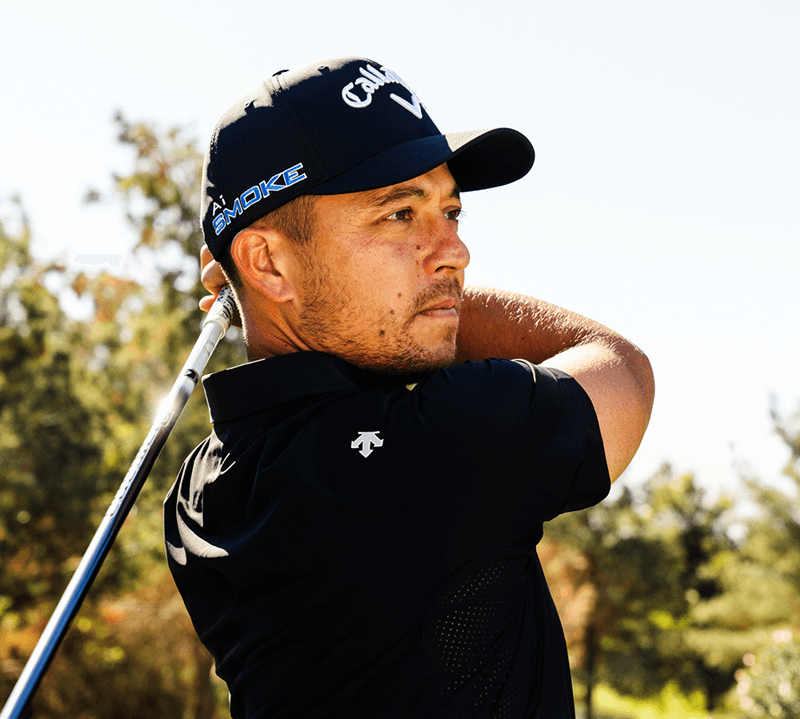 Xander in black Descente outfit with Callaway cap and club, outdoors.